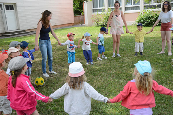 enfants font une ronde dans l'herbe avec les animateurs