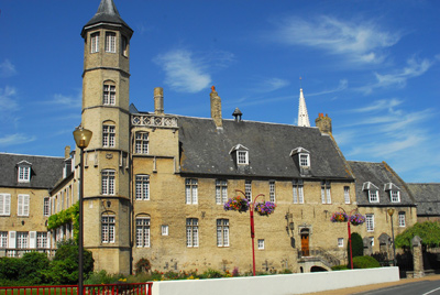 Grand château avec des murs blanc et une toiture noir, on voit une tour au premier plan